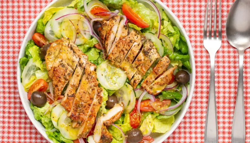 Deliciosa ensalada de pollo a la parrilla con lechuga, tomate, pepino, cebolla morada y aceitunas.