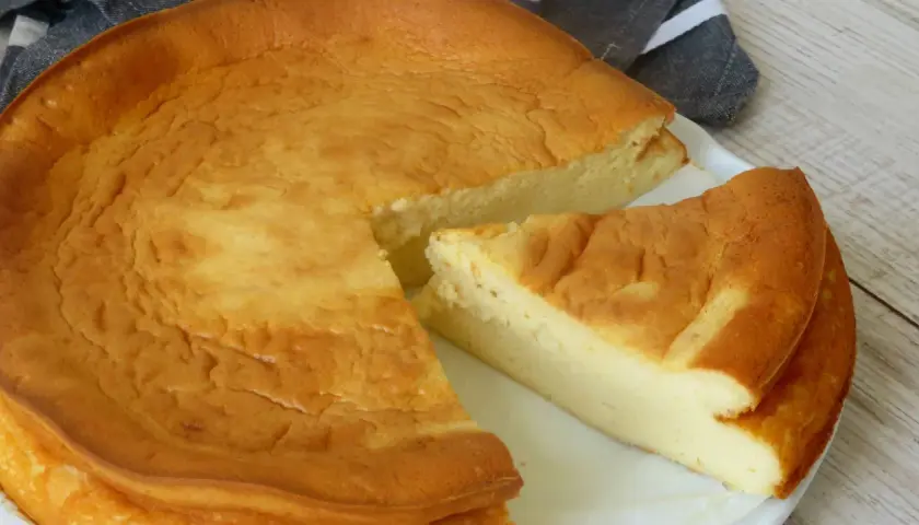 Tarta de queso Philadelphia dorada y esponjosa, con una porción cortada que revela su interior cremoso.