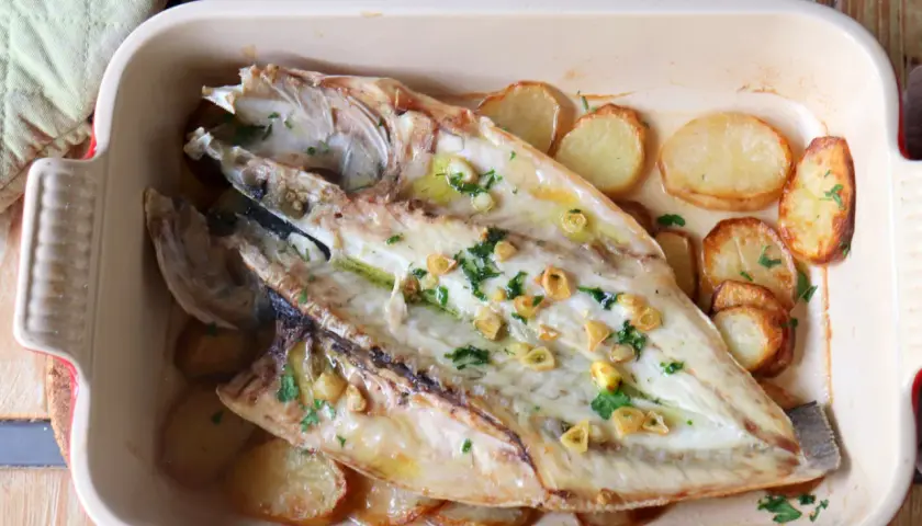 Lubina a la espalda horneada con patatas y ajo, lista para servir.