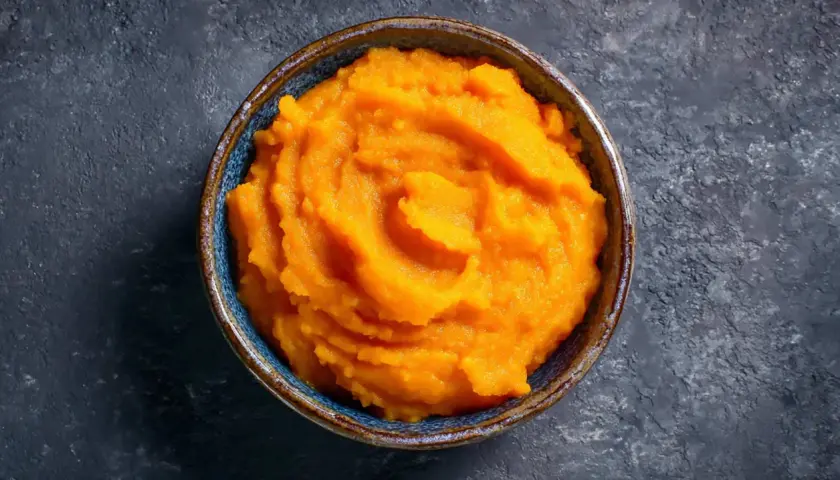 Un cuenco de cremoso puré de boniato, con su vibrante color naranja, listo para ser disfrutado.