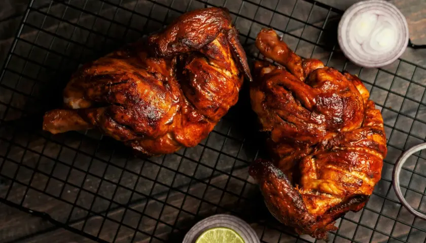 Dos jugosos pollos a la brasa, dorados y listos para disfrutar, acompañados de rodajas de cebolla roja y limón.
