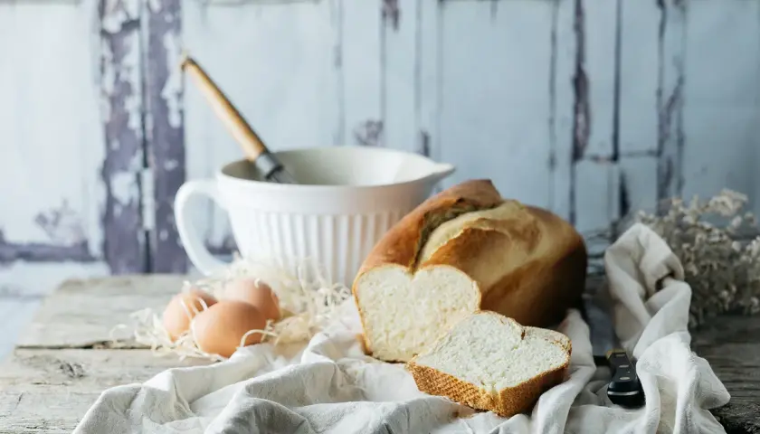 Pan brioche para torrijas, huevos y batidor sobre mesa rústica.