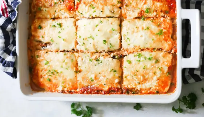 Una deliciosa lasaña de berenjena recién horneada, cubierta de queso derretido y perejil picado, lista para servir.