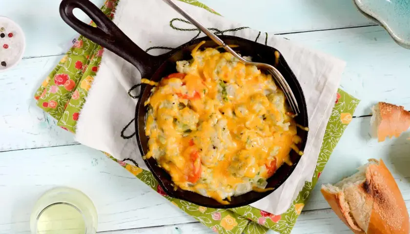 Coliflor gratinada burbujeante en sartén de hierro fundido, lista para disfrutar con pan crujiente.