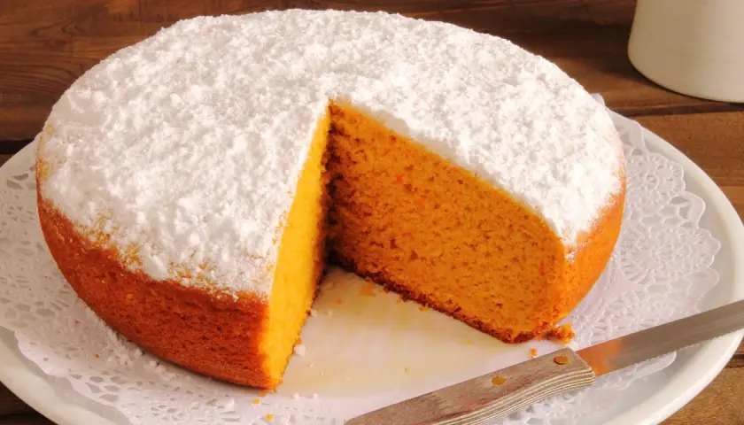 Pastel de zanahoria esponjoso, cubierto de azúcar glas, con una rebanada retirada.