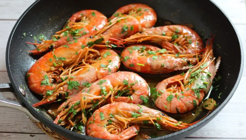 Gambones al ajillo chisporroteando en una sartén, con perejil fresco espolvoreado. ¡Un plato delicioso!