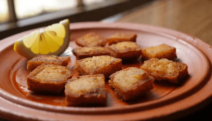 Deliciosos trozos de bacalao rebozado, dorados y crujientes, servidos en un plato de barro con una rodaja de limón.