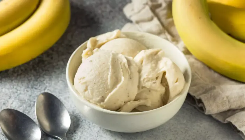 Un cremoso helado de plátano en un tazón blanco, con plátanos amarillos frescos al lado.