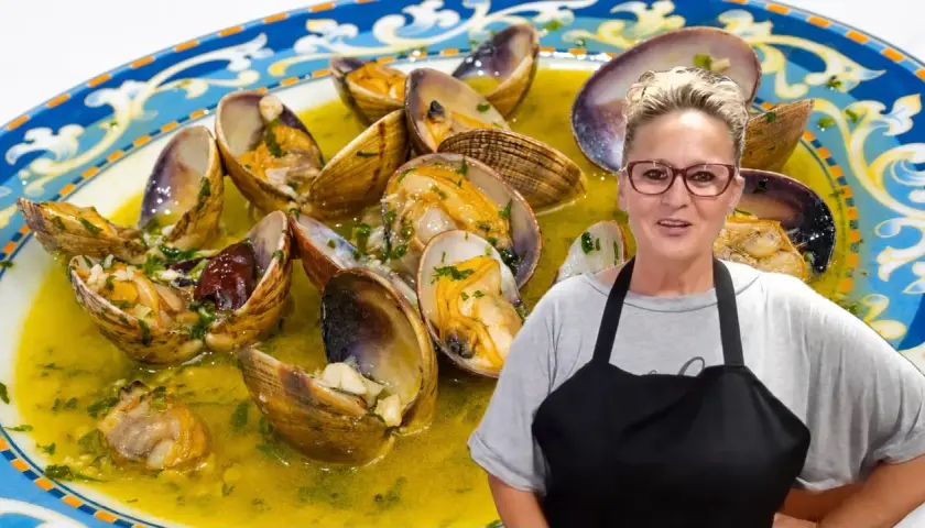 Una mujer sonriente presenta un plato de almejas al ajillo, conchas abiertas en una salsa dorada con perejil picado.