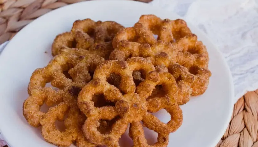 Un plato blanco con varios buñuelos de viento espolvoreados con canela y azúcar.
