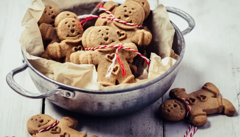 Un cuenco lleno de galletas de jengibre con forma de hombrecito, algunas atadas con hilo rojo y blanco.