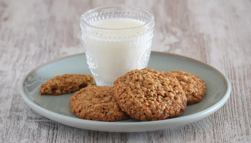 Un vaso de leche acompaña a unas deliciosas galletas de avena sobre un plato.