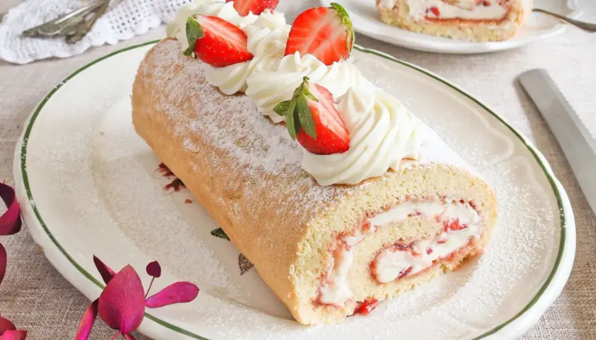 Un delicioso brazo de gitano con crema y fresas, espolvoreado con azúcar glas.