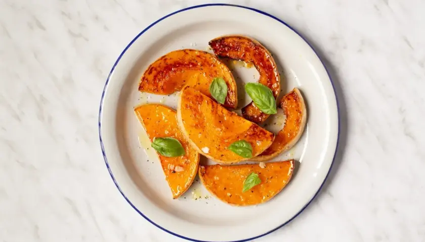 Rodajas de calabaza al horno, glaseadas y con hojas de albahaca fresca, servidas en un plato blanco con borde azul.