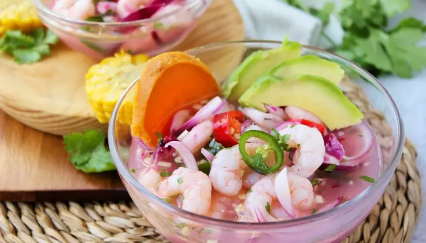 Delicioso ceviche de gambas con aguacate, cebolla morada, chile jalapeño y tomate. Servido en un cuenco de cristal, acompañado de maíz y cilantro fresco.