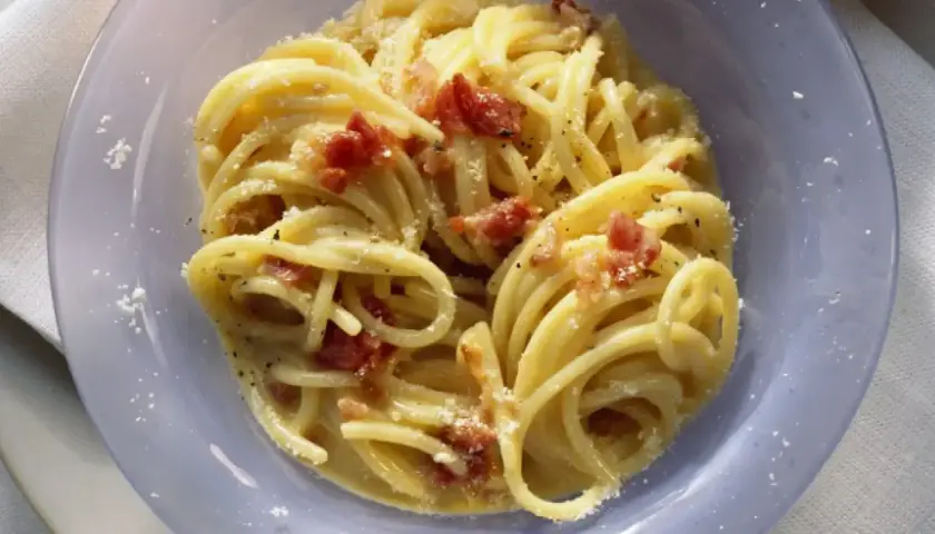Un plato de pasta carbonara cremoso con trozos de panceta crujiente y espolvoreado con queso rallado.