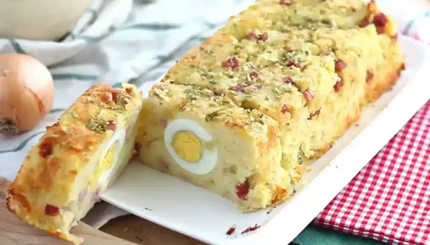 Un delicioso pastel de patata con trozos de bacon y huevos duros en su interior, espolvoreado con hierbas.