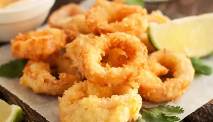 Crujientes calamars a la romana, dorados y listos para disfrutar, acompañados de gajos de limón y perejil fresco.