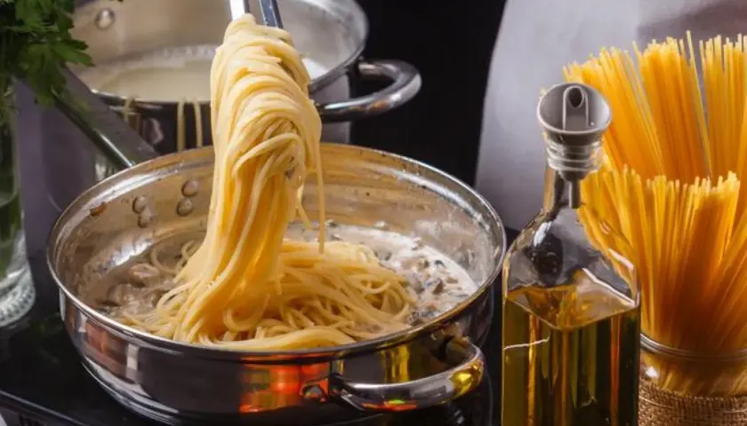 Unos espaguetis se añaden a una sartén con salsa cremosa, listos para convertirse en una deliciosa pasta al ajillo.