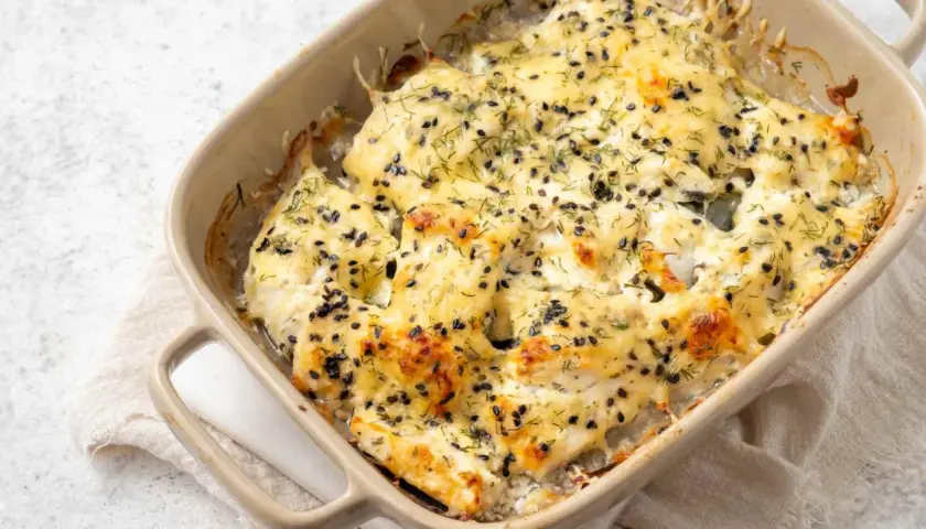 Bacalao a la nata gratinado, cubierto con semillas negras y eneldo, burbujeando en una fuente de cerámica.