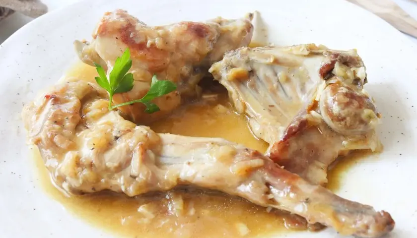 Deliciosas recetas de conejo guisado en salsa, servido en plato blanco con perejil fresco.