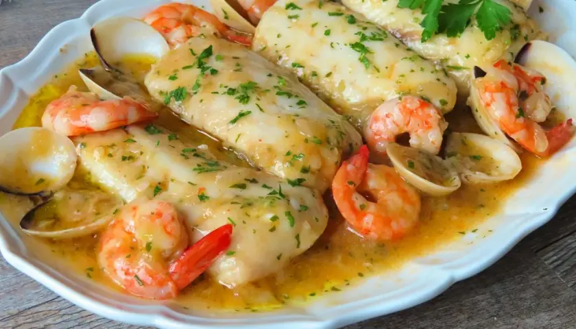 Merluza a la marinera con gambas y almejas, un plato delicioso bañado en salsa.