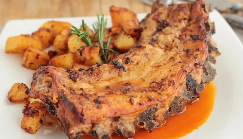 Costillas al horno con patatas doradas y romero fresco. Un plato jugoso y apetitoso.