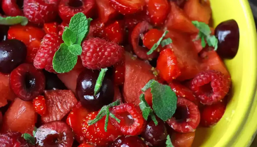 Delicioso postre con fresas, frambuesas, cerezas y menta en un tazón amarillo.