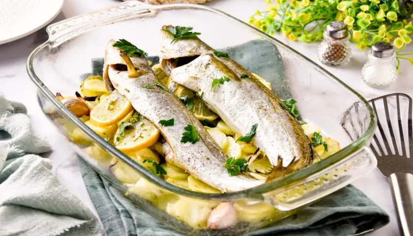 Pescadilla al horno con patatas, limón y ajo, recién salida del horno.