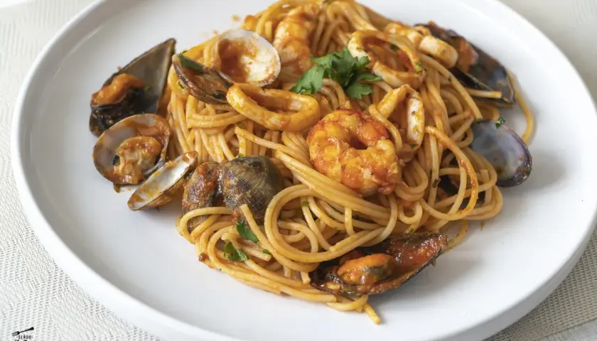 Espaguetis a la marinera con gambas, mejillones, almejas y calamares, servidos en un plato blanco.