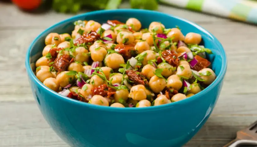 Ensalada de garbanzos fresca y colorida con tomate seco y cebolla morada en un cuenco azul.