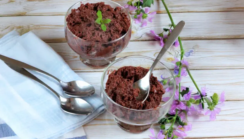 Dos copas de delicioso mousse de chocolate, decoradas con menta y flores moradas, listas para disfrutar.
