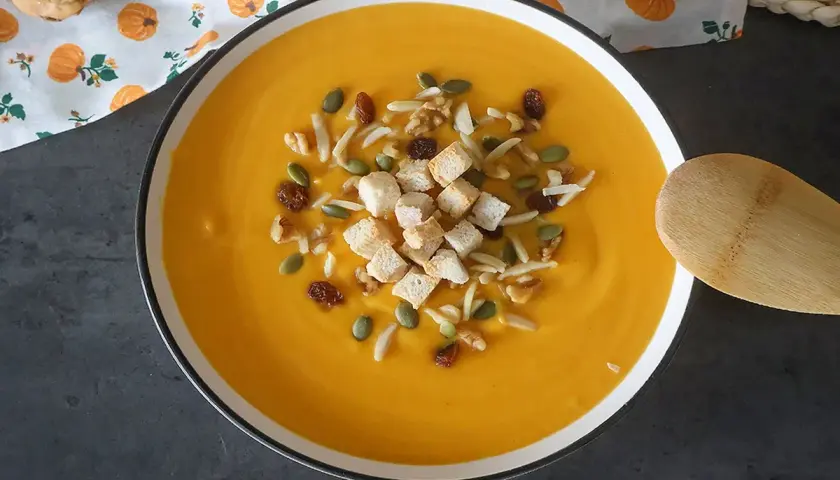 Un cremoso puré de calabaza adornado con picatostes, nueces, pasas y semillas de calabaza.