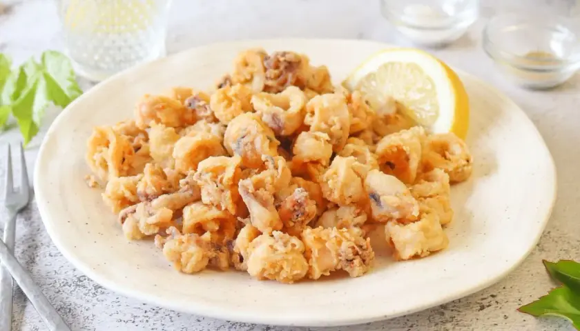 Un plato generoso de chipirones fritos crujientes, adornado con una rodaja de limón.
