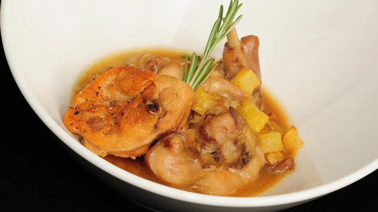 Delicioso conejo en salsa con patatas y romero, servido en un cuenco blanco.