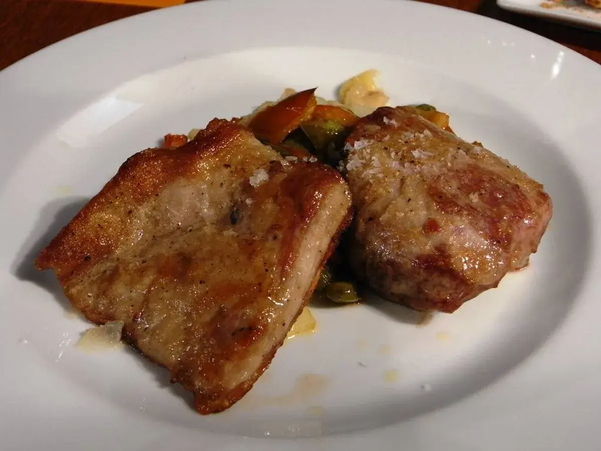 Dos trozos de secreto de cerdo a la plancha, dorados y jugosos, servidos con verduras salteadas en un plato blanco.