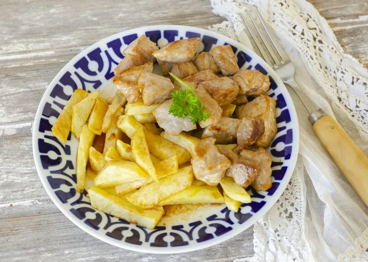 Raxo gallego jugoso con patatas fritas crujientes, servido en un plato con borde azul y blanco.