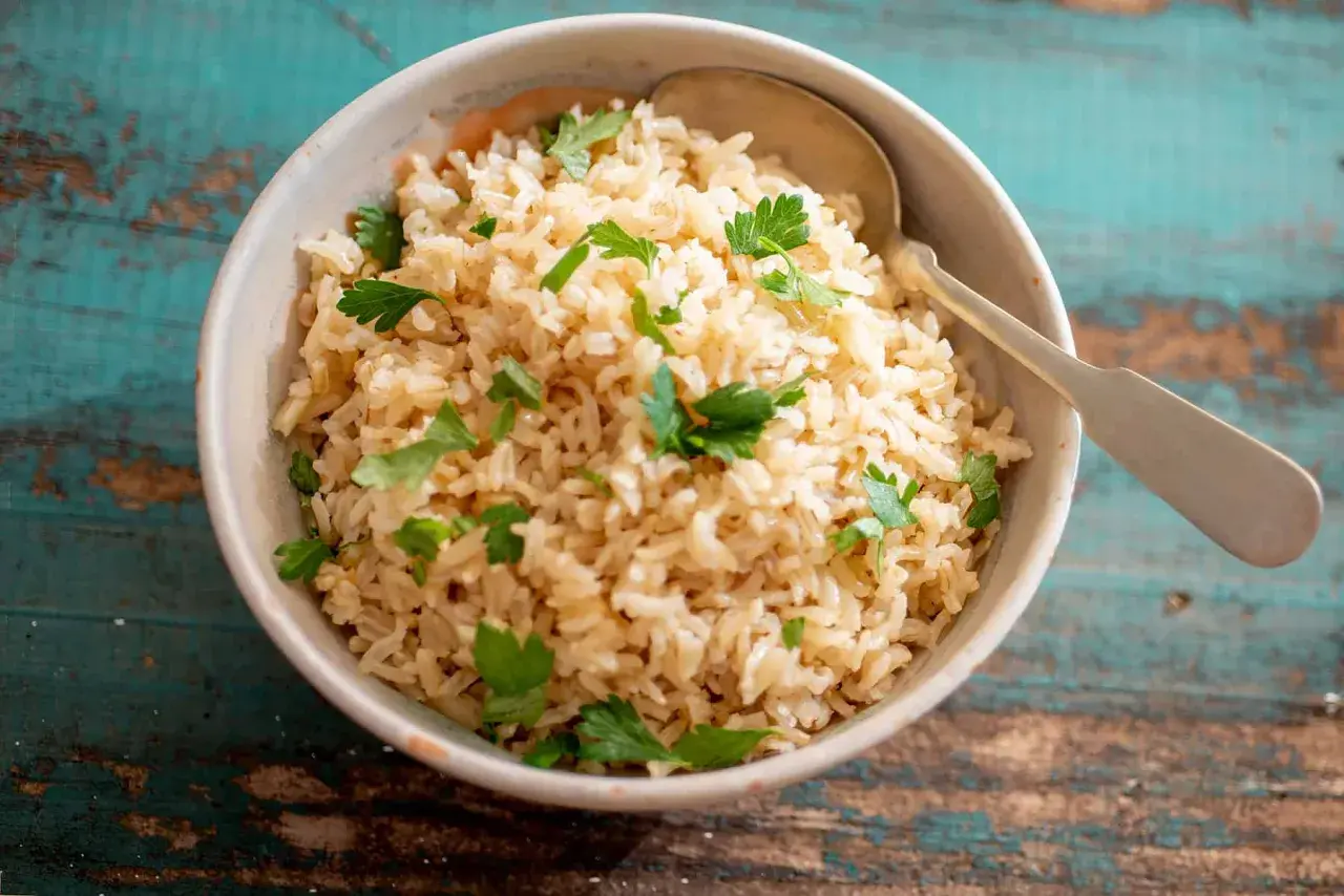 Un tazón de arroz integral esponjoso, perfecto para aprender como hacer arroz integral. Decorado con perejil fresco y una cuchara lista para servir.