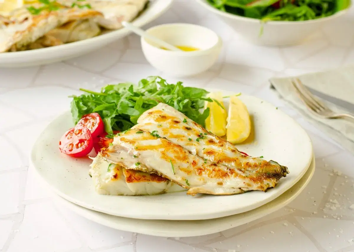 Deliciosa corvina a la plancha, servida con rúcula fresca, tomates cherry y gajos de limón. Un plato ligero y sabroso.