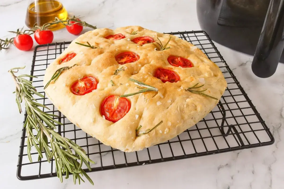 Focaccia receta casera con tomates cherry y romero sobre una rejilla.