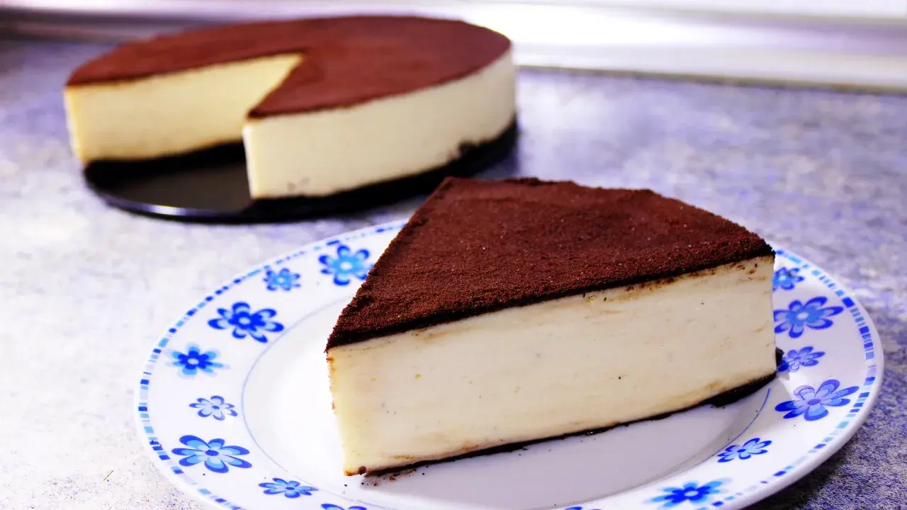 Un delicioso pastel de queso cubierto de cacao, perfecto para postres fáciles. Una rebanada servida en un plato con flores azules.