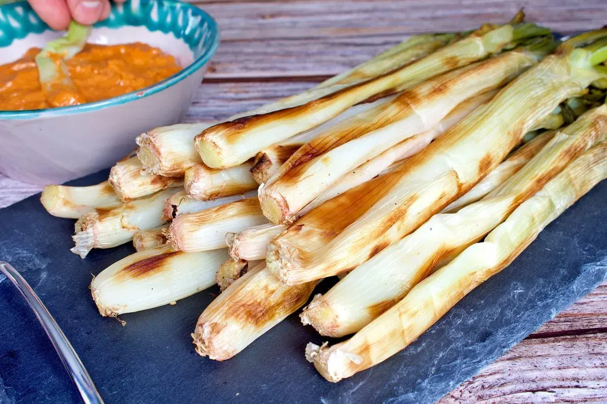 Calçots al horno, tiernos y dorados, listos para mojar en salsa romesco. Un festín de sabor.