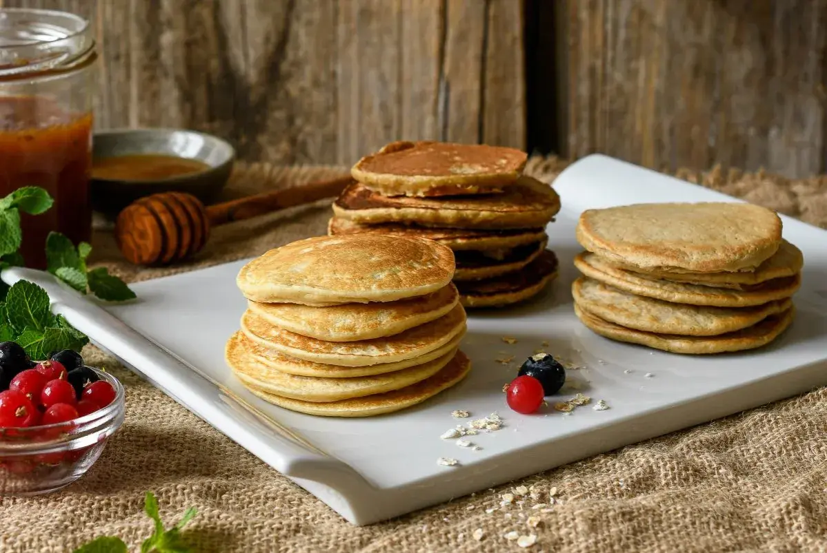 Montón de tortitas de avena doradas, servidas con bayas frescas y miel.