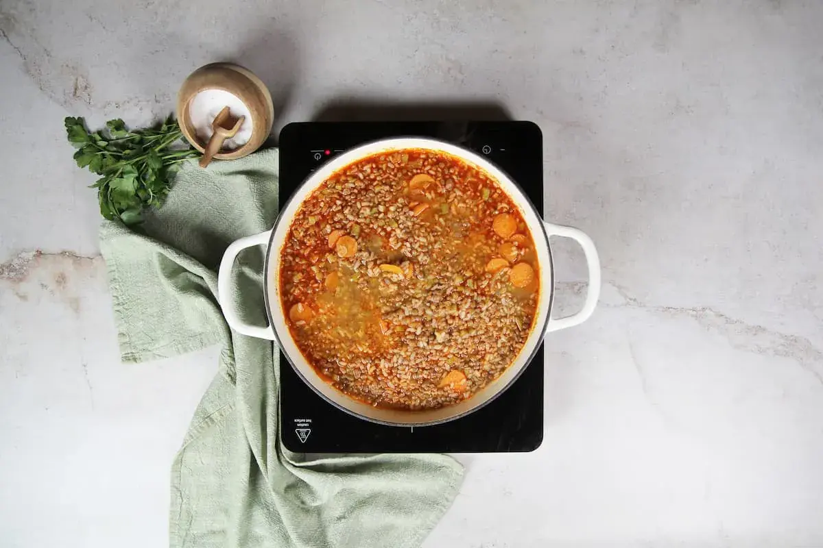 Olla con lentejas con arroz y zanahoria hirviendo. Al lado, perejil fresco y un cuenco de sal.