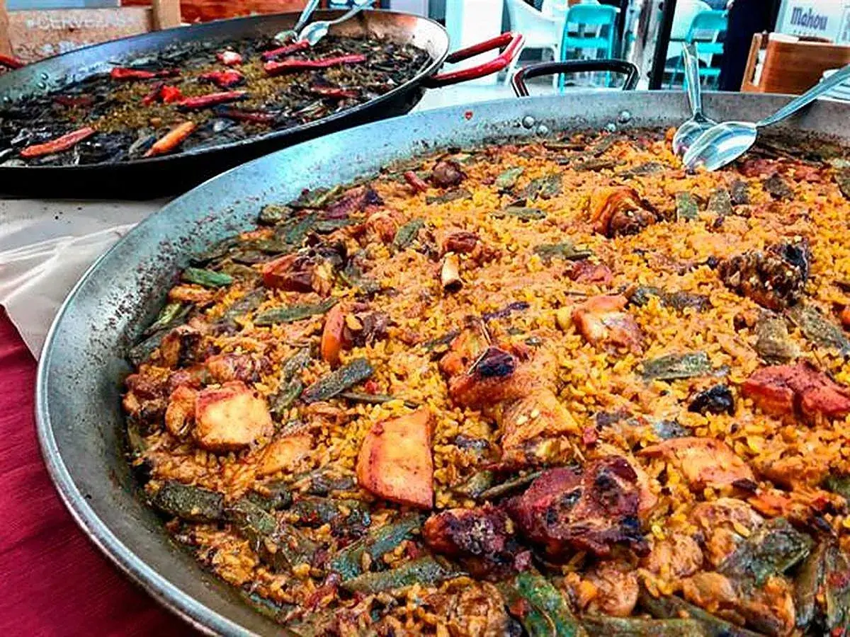 Paella valenciana con pollo, conejo y verduras. Los ingredientes se mezclan con el arroz en esta gran paellera.