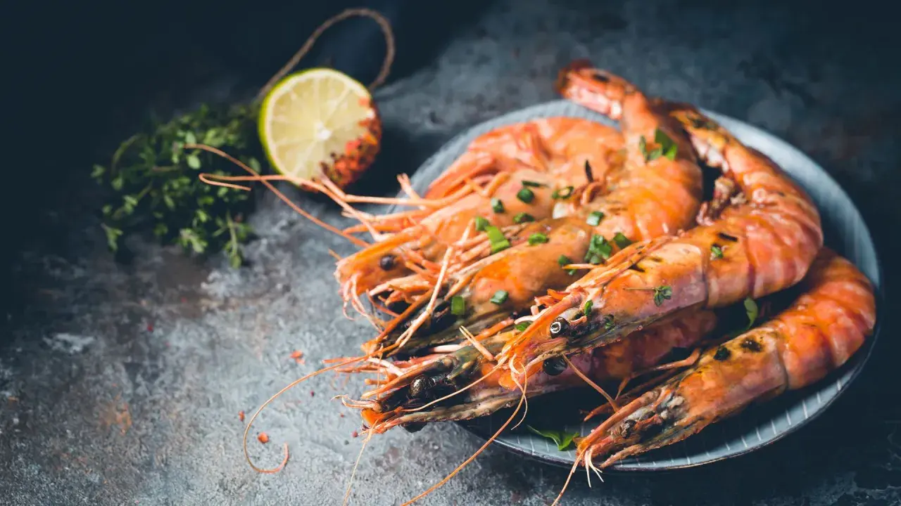 Gambones al horno, jugosos y dorados, servidos con hierbas frescas y rodaja de limón.