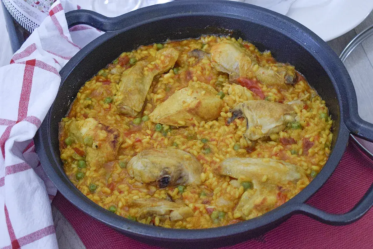 Un delicioso arroz con pollo en paellera, con trozos de pollo dorado, guisantes y pimientos rojos.