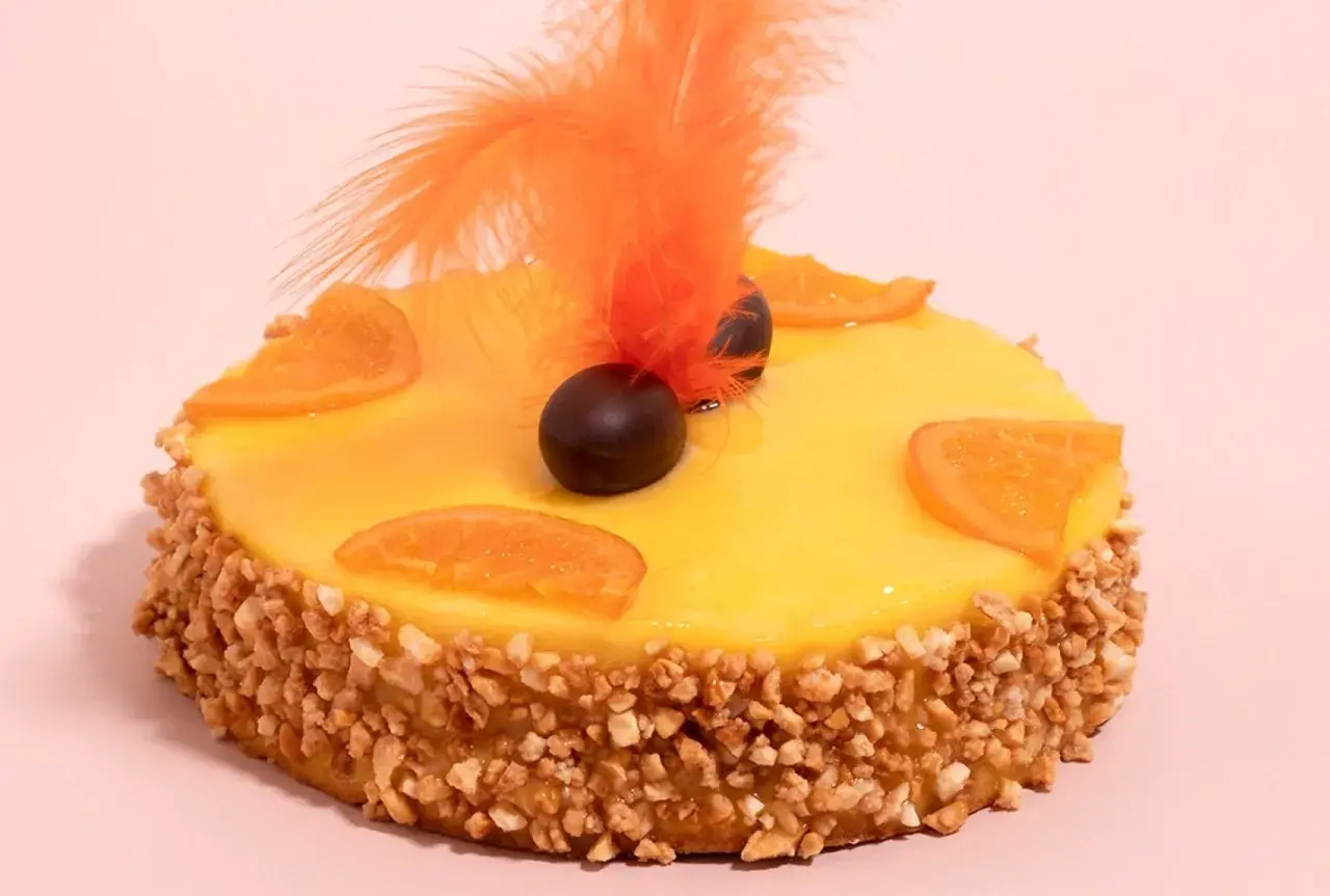 Deliciosa mona de Pascua catalana con glaseado amarillo, rodajas de naranja, chocolate y plumas naranjas.