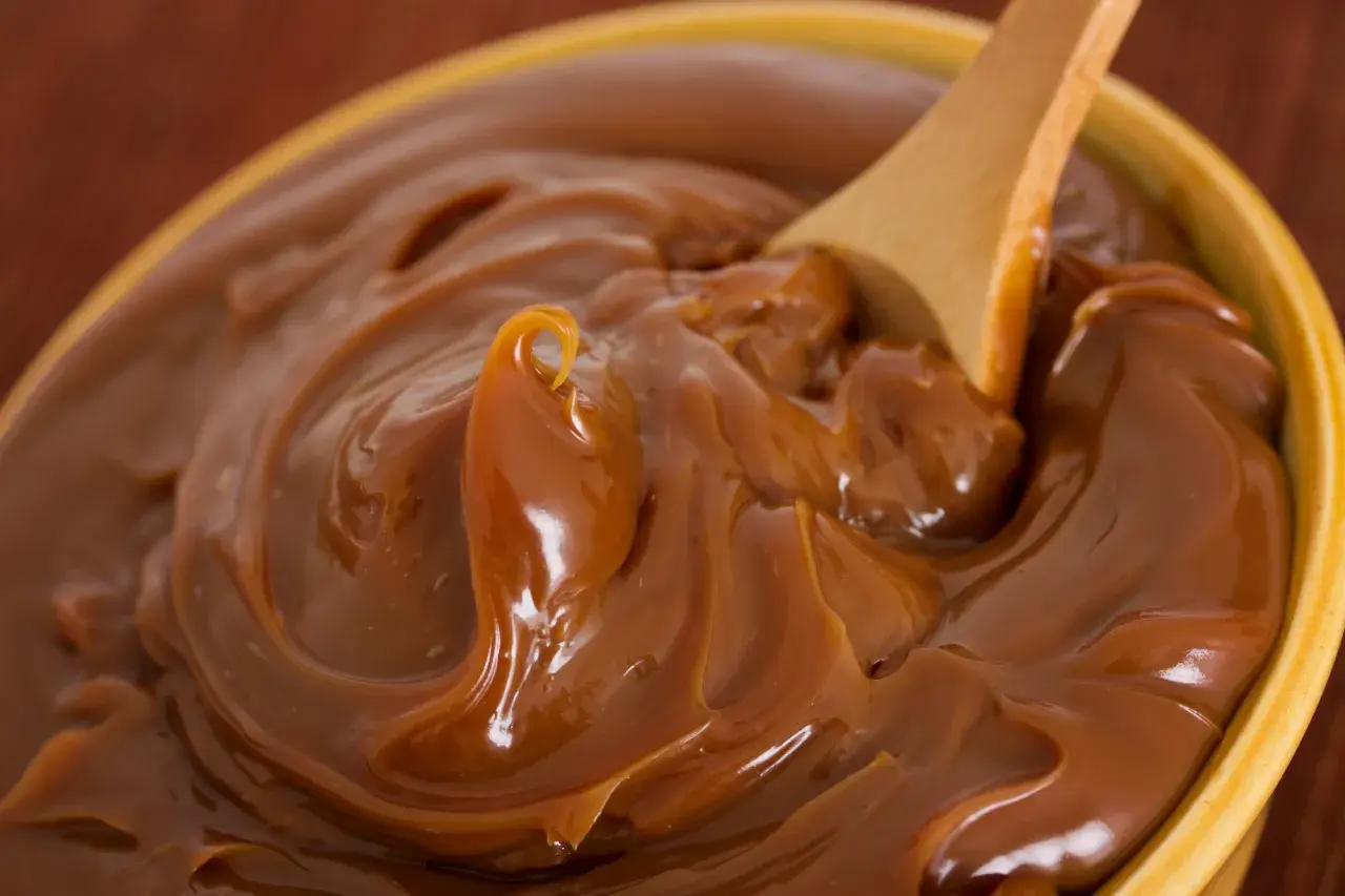 Cuchara de madera removiendo un tazón lleno de dulce de leche cremoso, perfecto para tu dulce de leche receta.