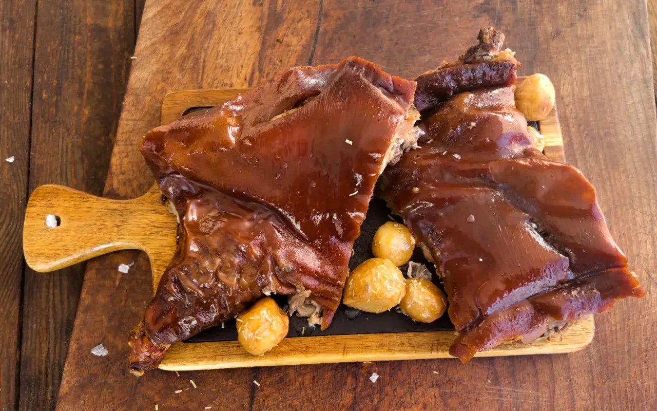 Delicioso cochinillo al horno, receta de la abuela, servido con patatas asadas sobre tabla de madera.